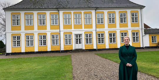 Katrine Carlsson foran Sandbjerg Gods. Slotsgården er godt fyldt op med håndværkerbiler, da der pågår en større renovering. Foto Ingrid Johannsen