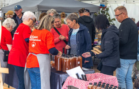 Frivillige i røde trøjer og gæster samlet ved en bod med æbleprodukter på Gråsten Æblefestival