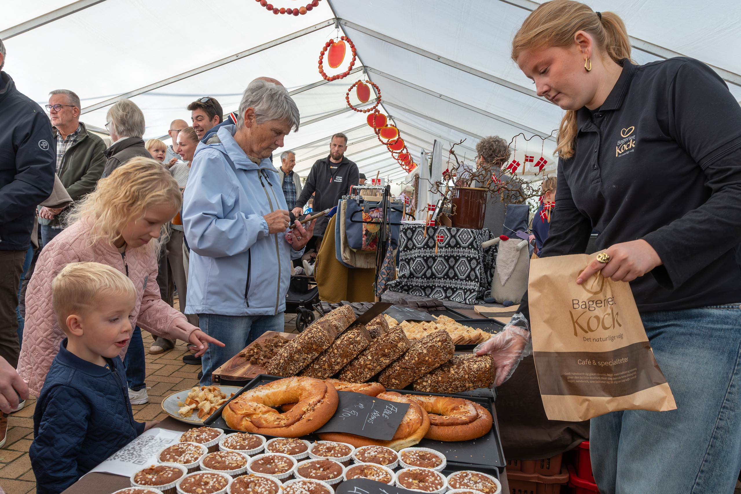 Ung kvinde sælger brød og kager til gæster i en bod på Gråsten Æblefestival