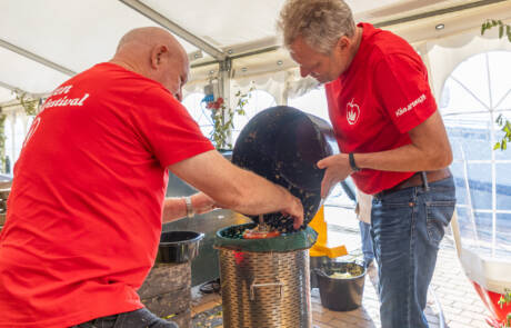 To frivillige i røde trøjer arbejder ved en æblepresse på Gråsten Æblefestival
