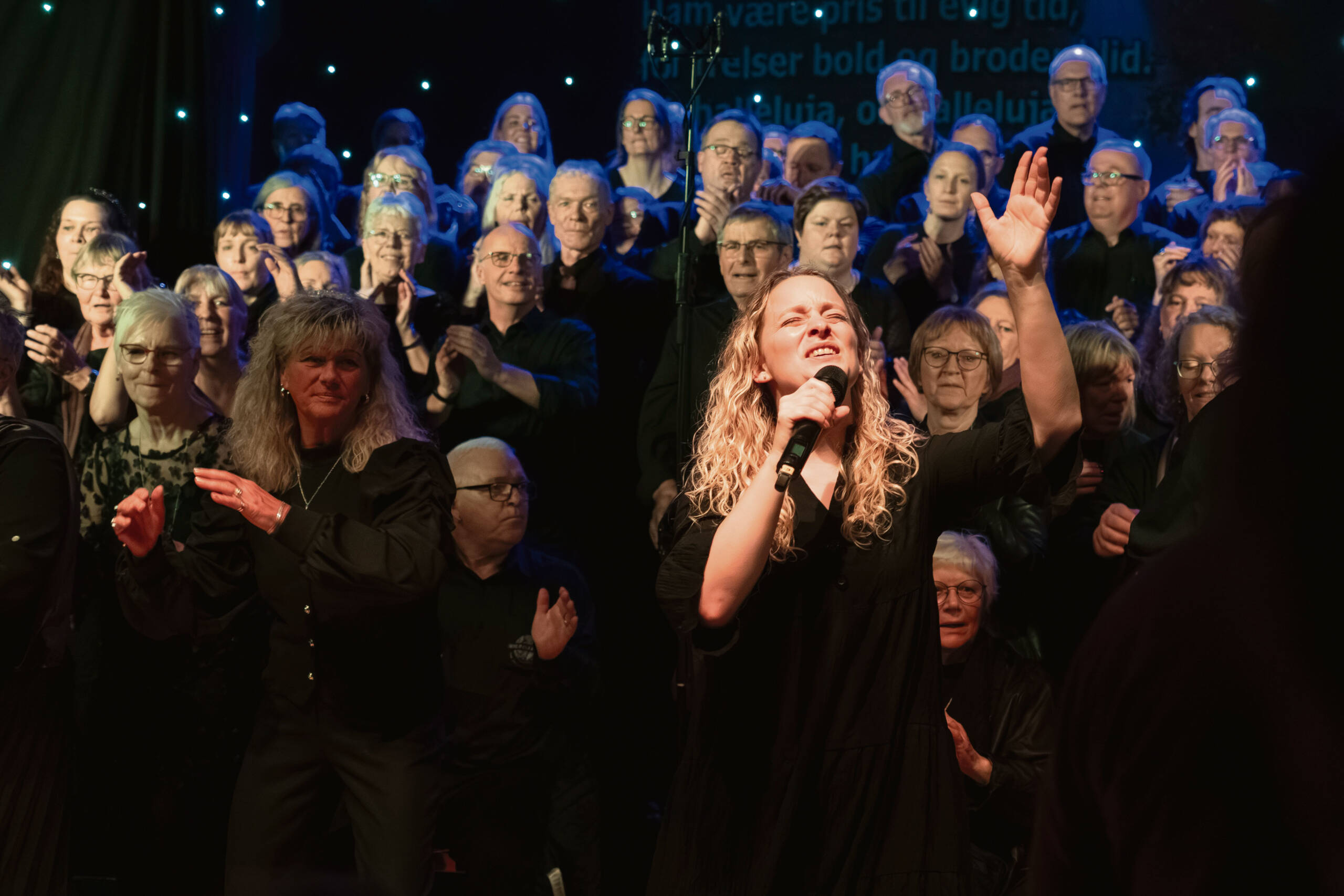 Gospelkoret Gospel Oaks synger på scenen med en kvindelig solist i front
