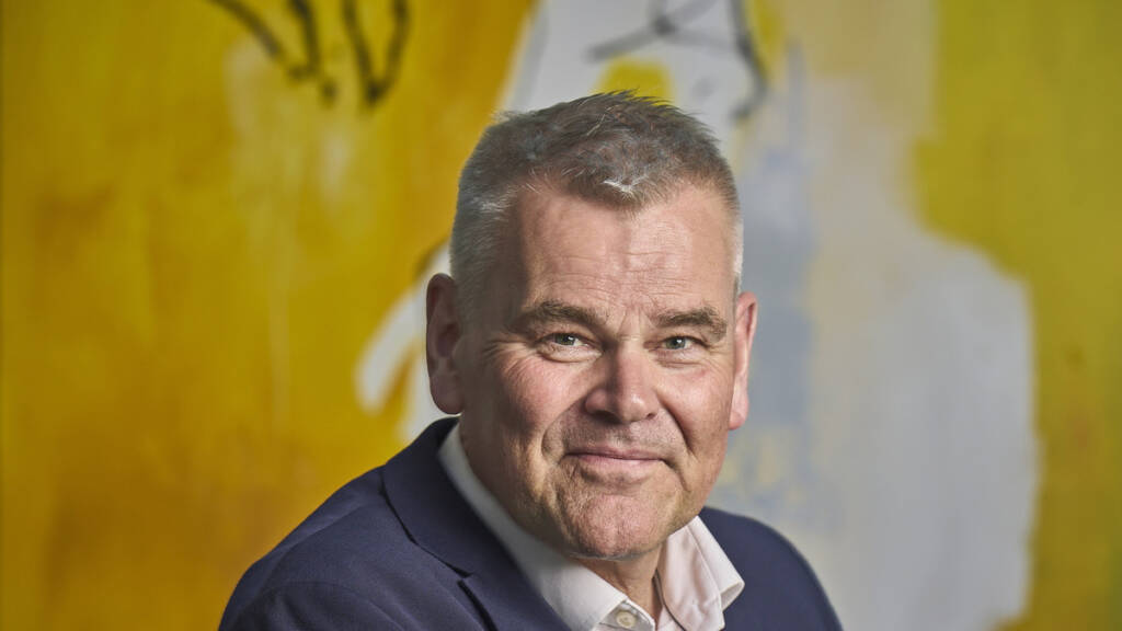 Portræt af smilende mand i mørkeblå jakke foran en gul væg