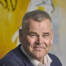 Portræt af smilende mand i mørkeblå jakke foran en gul væg