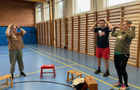 Parkour og crossfit hitter i Gråsten – billede 7 Tre deltagere i en gymnastiksal løfter hænderne op mod hovedet foran ribbevægge