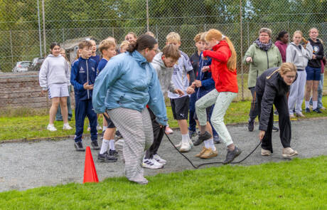 Børn og voksne i gang med en aktivitet på en grusbane ved et hegn