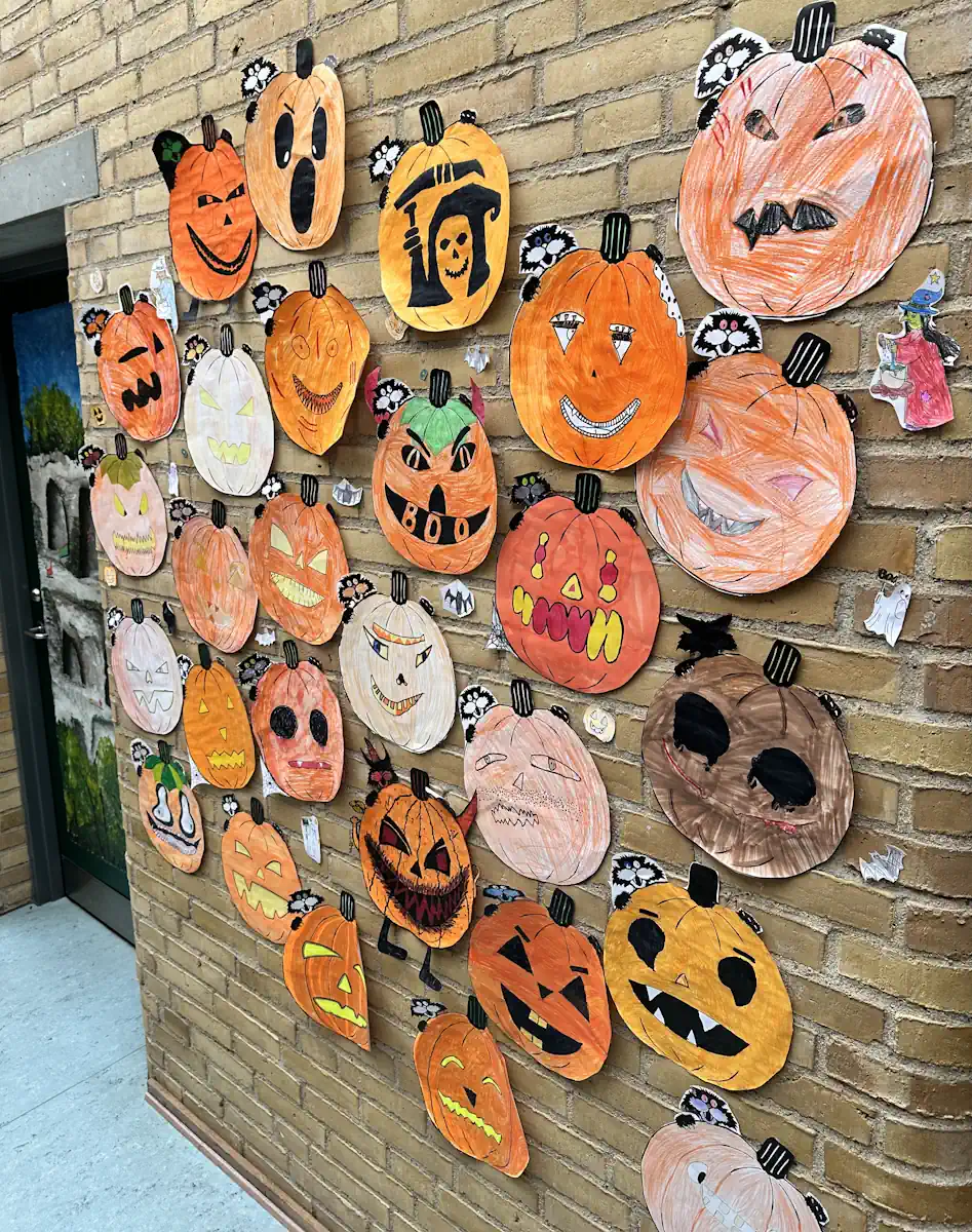 Børnetegninger af halloweengræskar hængt op på en murstensvæg på Grænseegnens Friskole