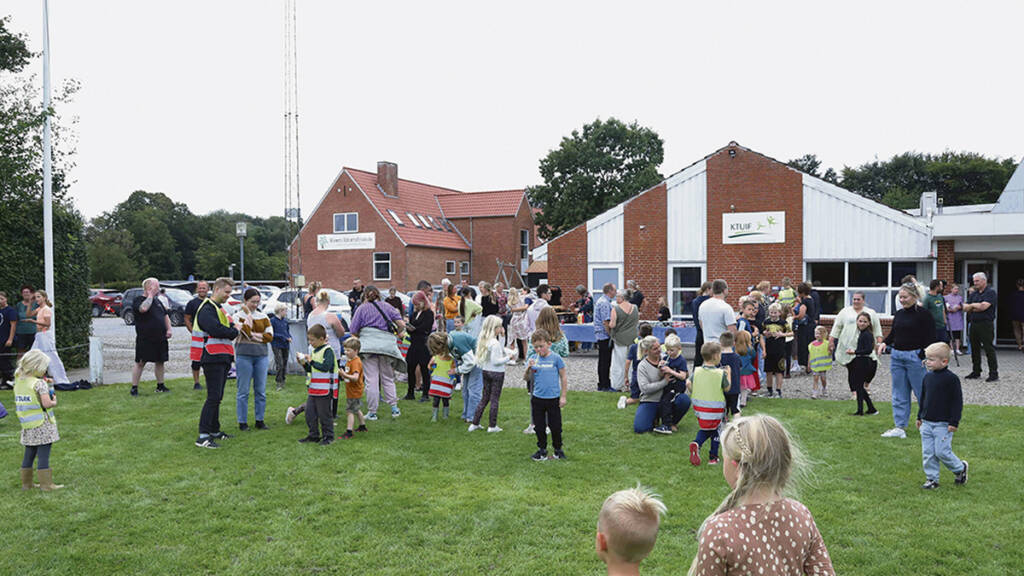 Børn og voksne er samlet på græsplænen foran bygningerne ved Kværs Idrætsfriskole.
