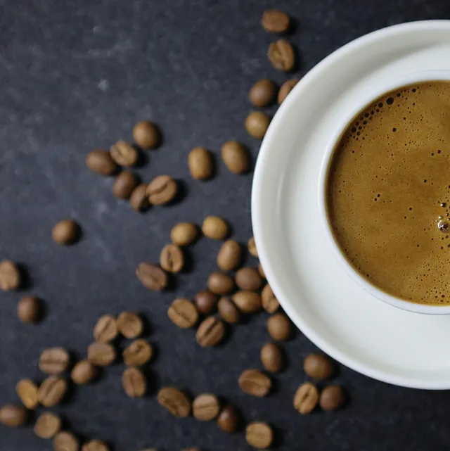 Kop sort kaffe på et mørkt bord med spredte kaffebønner