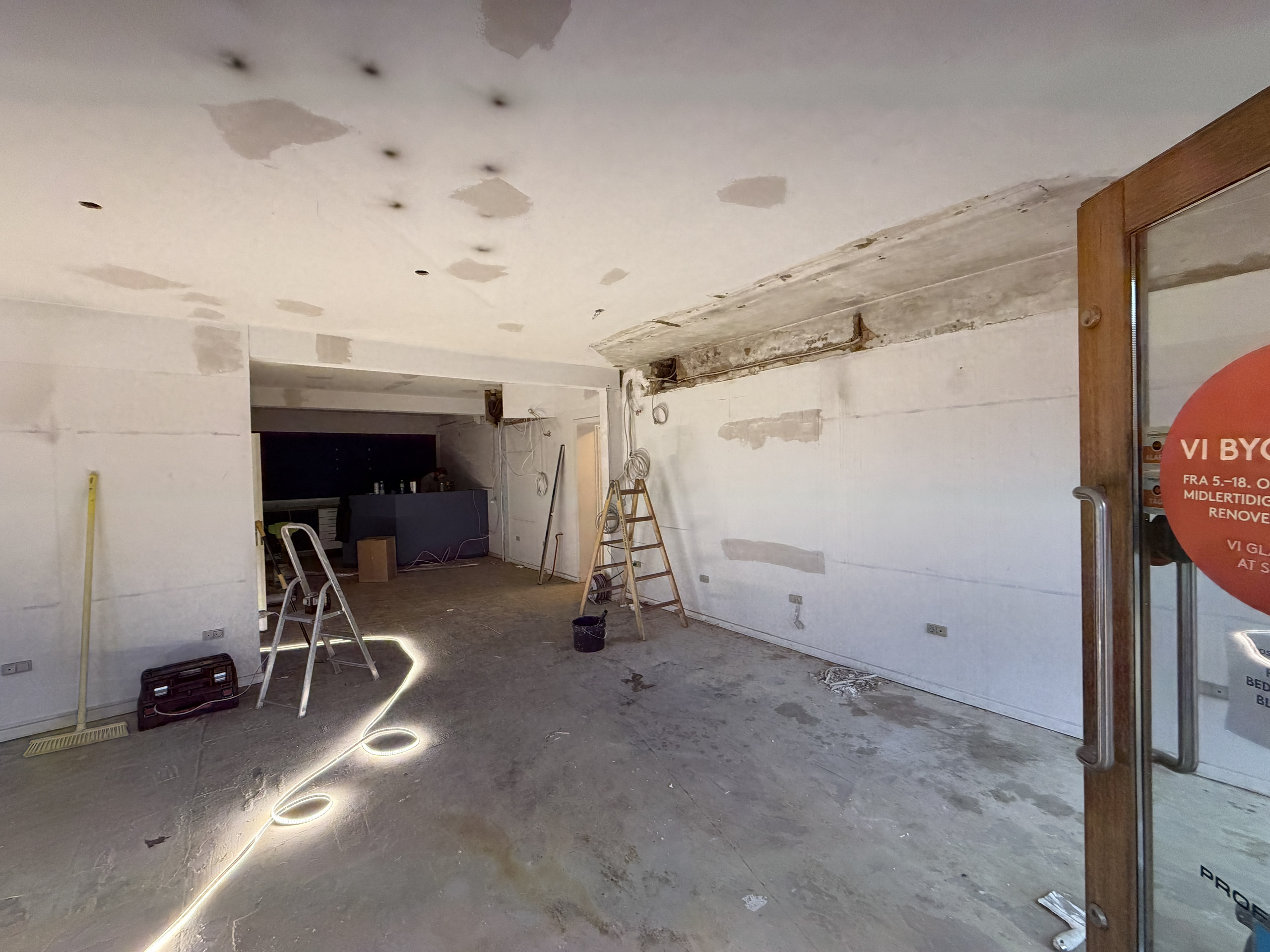 Orange balloner og romkugler ved genåbning af Profil Optik – foto 2 Tomt butikslokale med afskallet loft, en stige og blottede vægge under renovering