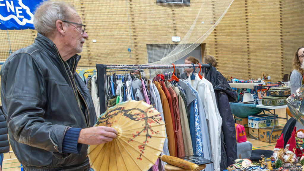 Mand i skindjakke holder en solparaply op ved et loppemarkedsbord i hallen i Ahlmannsparken