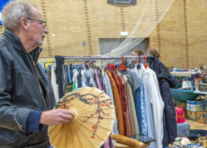 Mand i skindjakke holder en solparaply op ved et loppemarkedsbord i hallen i Ahlmannsparken
