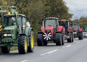Lang række traktorer i konvoj på en landevej, forrest en grøn og en rød traktor