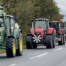 Lang række traktorer i konvoj på en landevej, forrest en grøn og en rød traktor