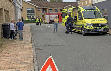 Advarselsskilt med teksten Brand på vejen foran ambulance og brandbil i Domhusparken